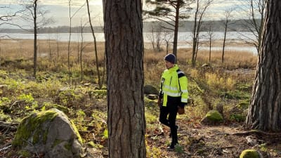 Man i gul jacka går genom skog, hav i bakgrunden.