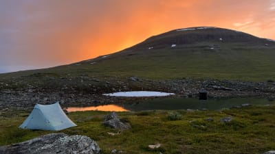 Vaalea teltta tunturi auringonlaskun aikaan.