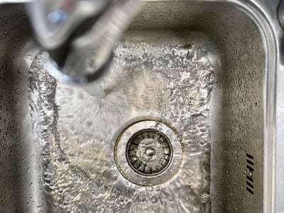 Vatten rinner från en kran ned i en diskho av stål.