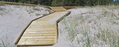 Ett promenadstråk i trä, byggt bland sanddynerna på en strand. 