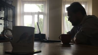 Anthony Goltz sitter i mörkret vid sin bärbara dator med ljusa fönster i bakgrunden