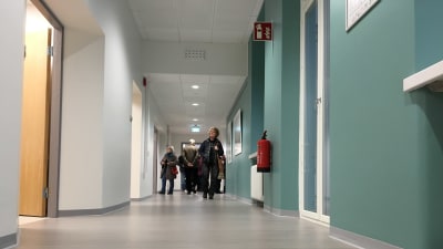 Människor i en korridor med grått golv och turkosa väggar.