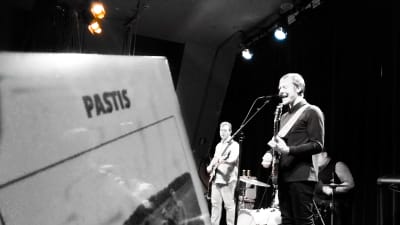 Bandet Pastis vinylskiva i förgrunden och sångaren Markus Nymalm i bakgrunden live på scen.