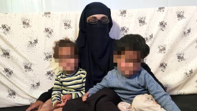 En norsk terrormistänkt kvinna och hennes två barn sitter tätt ihop. Barnens ansikten är blurrade.
