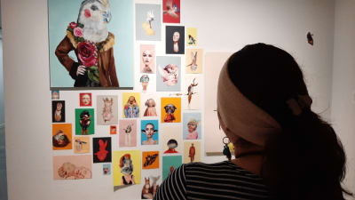 Bessie Reyes, en dam med hästsvans och gult band kring håret, står och tittar på konst på en utställning.