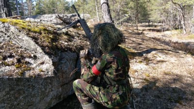 En airsoftspelare är på sin avkt bakom en sten.