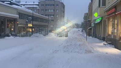 En fronlastare plogar snö i centrum av en liten stad. 