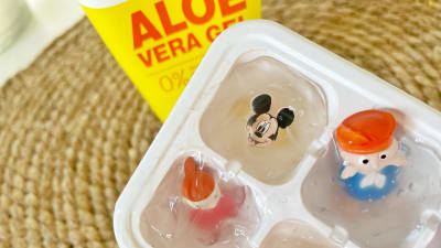 En iskubsform fylld med aloe vera-gel. En flaska med aloe vera står intill och iskubsformen ligger små plastfigurer insatta i gelen.