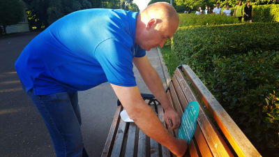 Vasilij Grjaznov limmar klistermärken med uppmaning att hålla avstånd också på parkbänkarna.