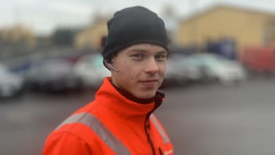En ung man med mössa och headset är klädd i orangea arbetskläder