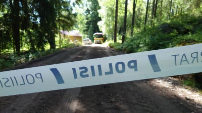 Ett polisband går över en sandväg med träd på ömse sidor. I slutet av vägen skymtar ett hus och en brandbil.