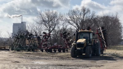 Traktor på bondgård i Kansas i solsken, gödselfabrik med skorsten i bakgrunden.