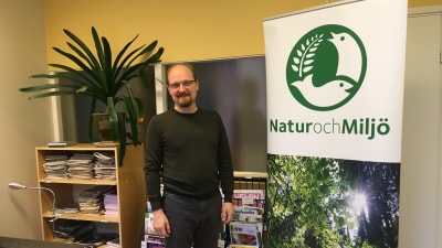 En man står bredvid en krukväxt på ett kontor.