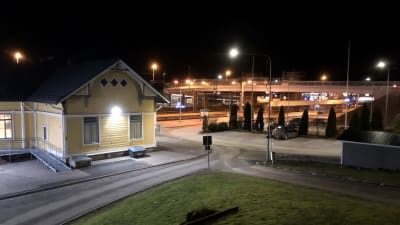 En gul träbyggnad intill järnvägsspår och en bro.