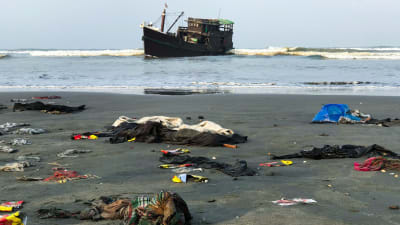En del av de räddade rohingyernas ägodelar låg kvar på stranden nära Teknaf på torsdag morgon. Det är oklart om trålaren i bakdrunden är den båt som de drivit omkring på i nästan två månader. 