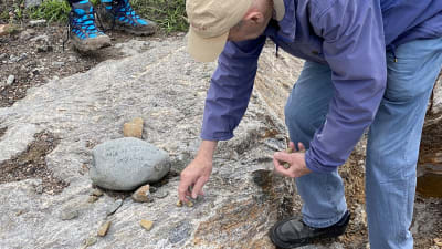 En sten med text på ligger på berggrunden. En man plockar upp små stenar.