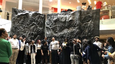 Grupperna samlas i museets aula framför en stor svart skulptur föreställande USAs landmassor och folk.