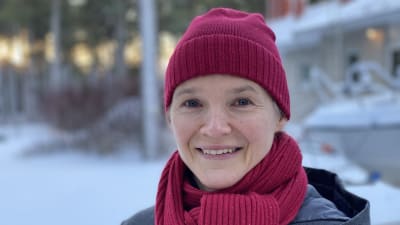 Kvinna i röd mössa och röd halsduk står i ett vintrigt landskap.