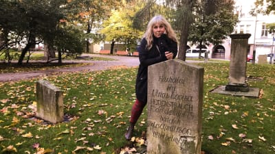 Stina Wollter står lutad över en gravsten i Petsparken