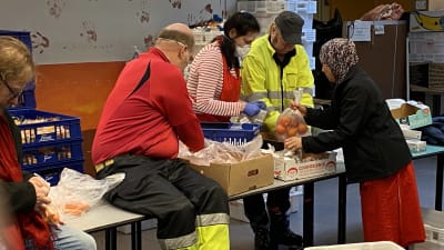Ett flertal personer i arbetskläder packar ner matvaror i plastpåsar. 