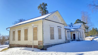 En ljus större träbyggnad med vanerskivor på fönstren. Snö, solsken.