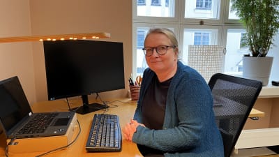 En kvinna i glasögon sitter vid ett skrivbord.