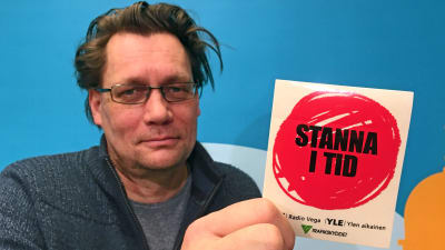 Mikael Kokkola visar upp ett klistermärke från kampanjen Stanna i tid.