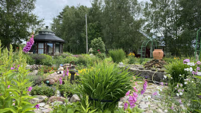 En trädgård med ett mörkt lusthus till vänster och en stenfontän till höger.