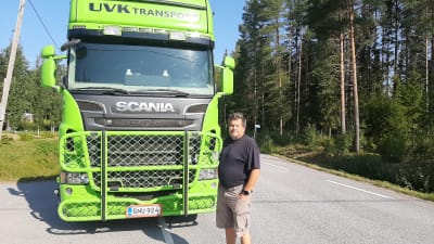En man i shorts står framför en grön lastbil. 