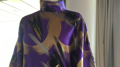 En lilafärgad sidenklänning med gulddetaljer.