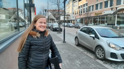 Kvinna med långt hår och svart jacka i stadscentrum.