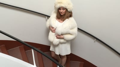 Emma Sandström står i en trappa i klädd vit pälsmössa, vit päls och klänning.