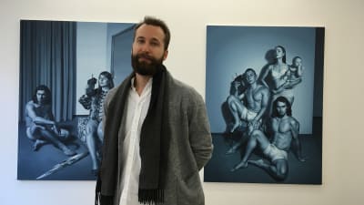 Man tittar in i kameran, två konstverk synns bakom honom