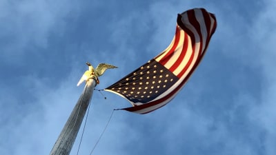 Amerikansk flagga på hög stång med örnprydnad i guld.