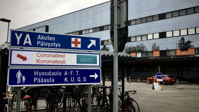 Skylt vid Vasa centralsjukhus där det står bland annat Coronatest. I bakgrunden syns teststället.