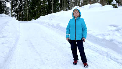 En kvinna i blå jacka står på en snötäckt väg i en skog.