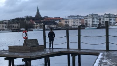 En person står på en brygga och ser ut över vattnet och Stockholm.