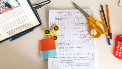 Studiematerial och ett anteckningsblock med matematiska formler på ett skrivbord.