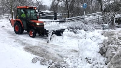 Liten traktor plogar snö på gångbanan.