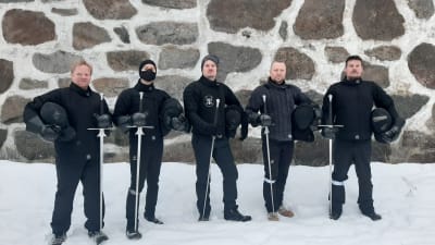 Fem män i svarta dräkter och med svärd.