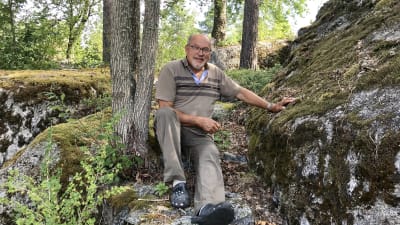 Svampplockaren Kurt Söderberg sitter mellan ett träd och en stor sten där han vanligtvis alltid brukar hitta kantareller. Nu syns inga svampar till.