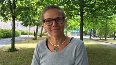 Kvinna med glasögon poserar vid träd