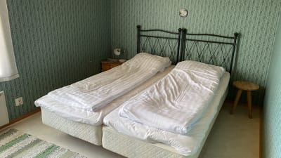 Två bäddade sängar i ett rum med grönmönstrad tapet.