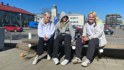 Tre flickor i tonåren sitter på en bänk i solskenet utanför Nickby huvudbibliotek. Två av dem tittar in i kameran och ler.
