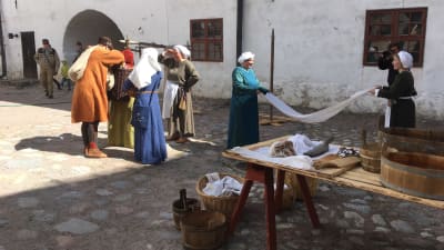 två kvinnor i medeltida dräkter tvättar byke på gården på Åbo slott under medeltidsevenemang. 