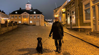 Barbro står på rådhustorget i Borgå med sin svarta hund.