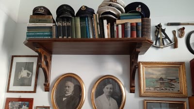 gamla fotografier i ramar och böcker och kaptenshattar på hylla
