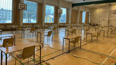 En tom gymnastiksal som gjorts om till skrivsal/studentskrivningar. Pulpeter och stolar på glesa avstånd och handsprit på varje bord.