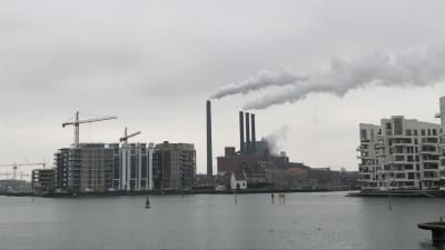 Fabrikspipor och moderna byggnader intill vattnet i Köpenhamn.