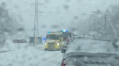 Ambulans och brandbil syns genom en snöig vindruta. Trafikolycka på Myrgrundsvägen i Vasa.